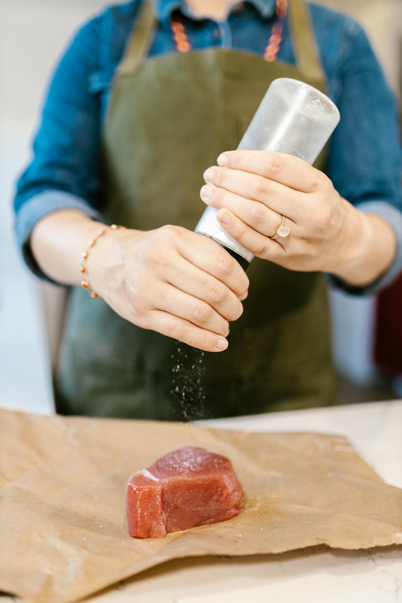Chef in apron seasoning raw red meat with salt for cooking.