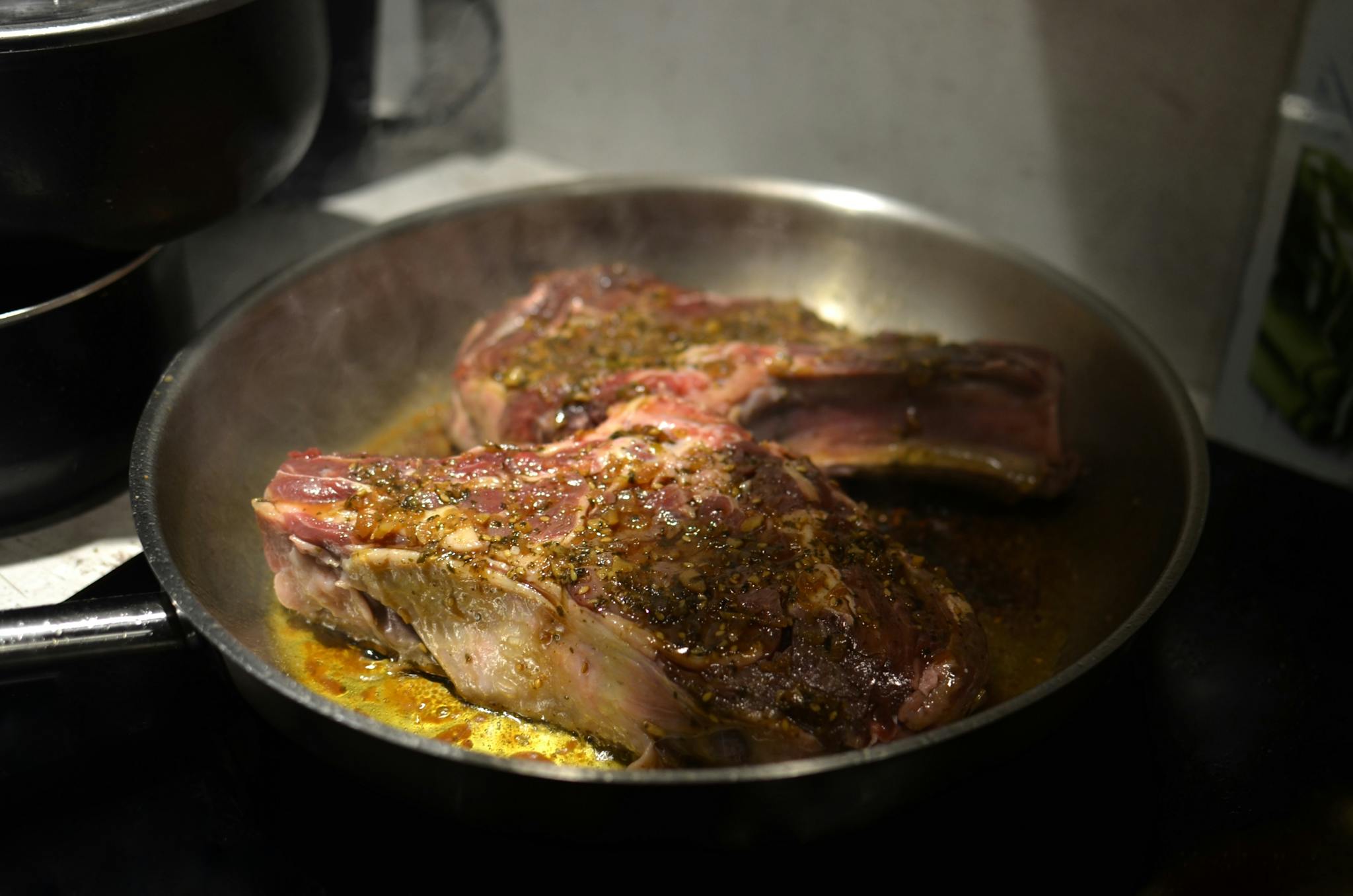 Close-up of seasoned beef steaks sizzling in a hot frying pan indoors.