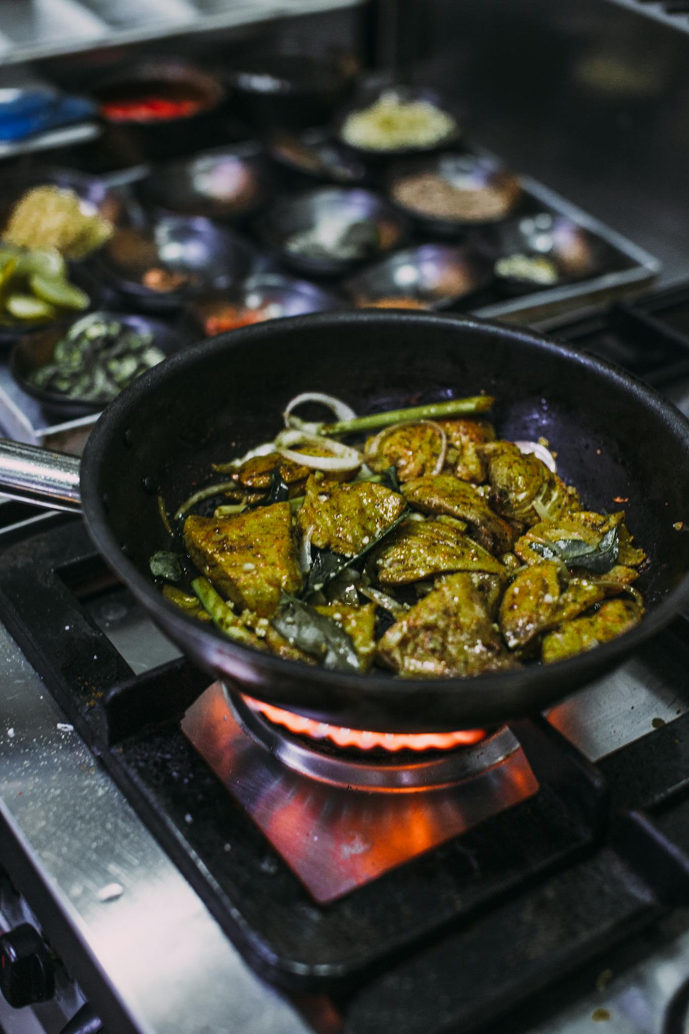 Close-up of spiced chicken sizzling in a pan over a flame, highlighting cooking process.